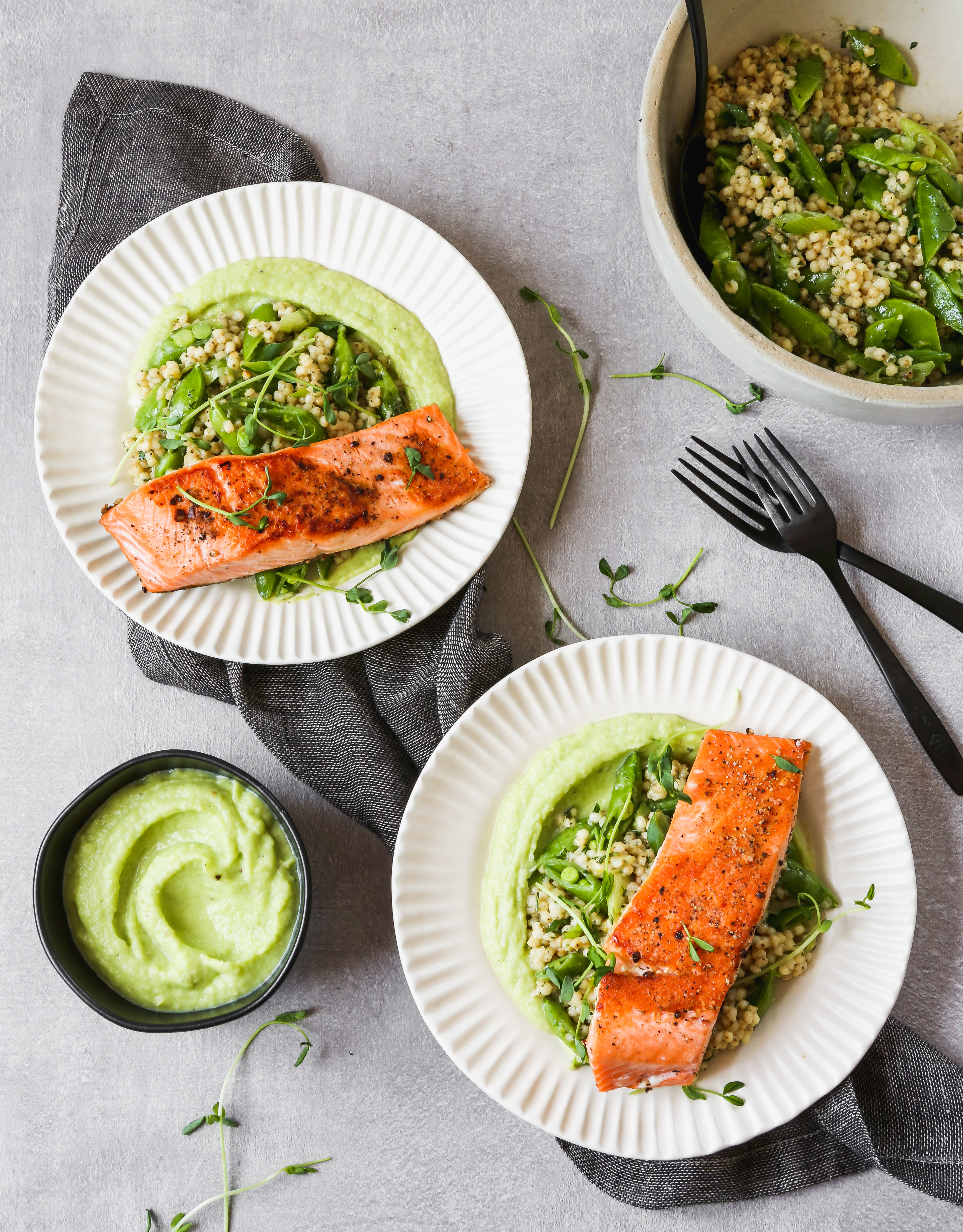 pan Seared salmon on white plates with green sauce and grain salad, set on a gray background.