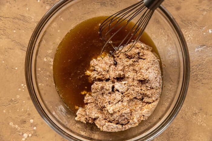 maple syrup and muffin batter in a glass mixing bowl with a whisk