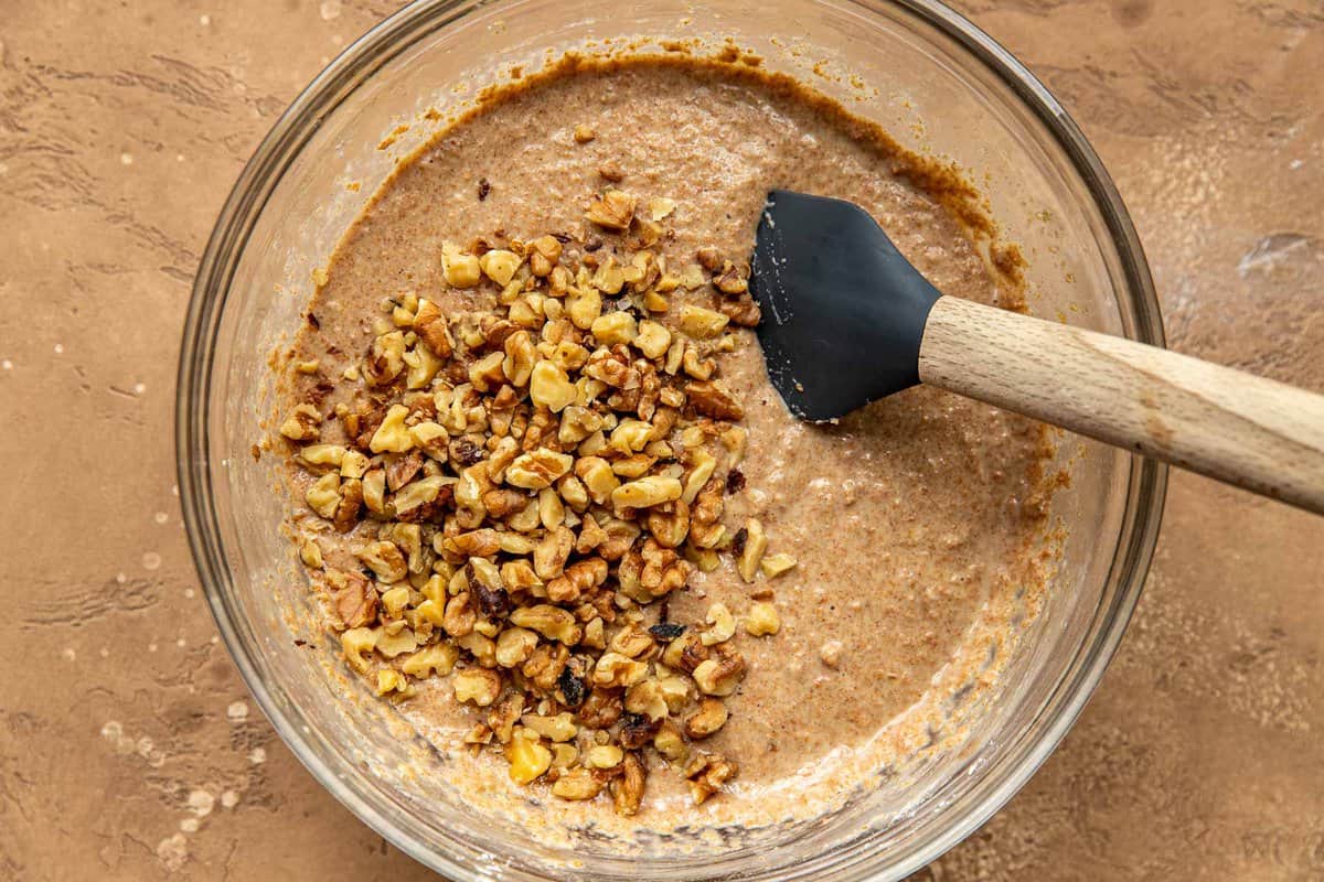 bran muffin batter in a glass mixing bowl with chopped walnuts added
