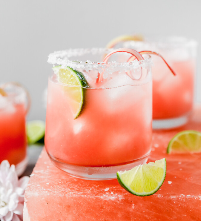 vibrant pink cocktail set on a pink salt block with lim wedges scattered around