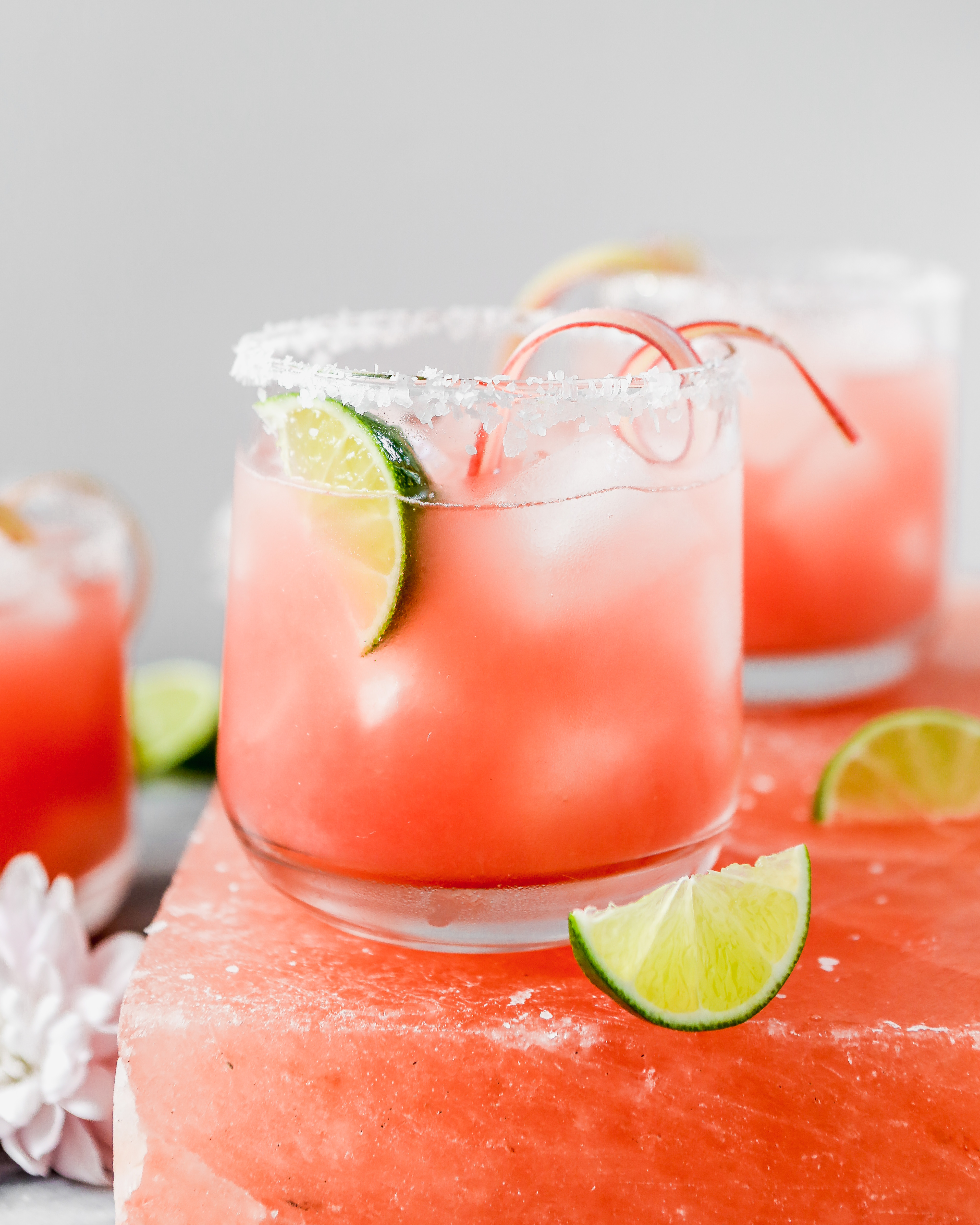 vibrant pink cocktail set on a pink salt block with lim wedges scattered around