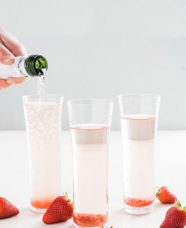 cocktail in tall flute glasses with strawberry slices on top.