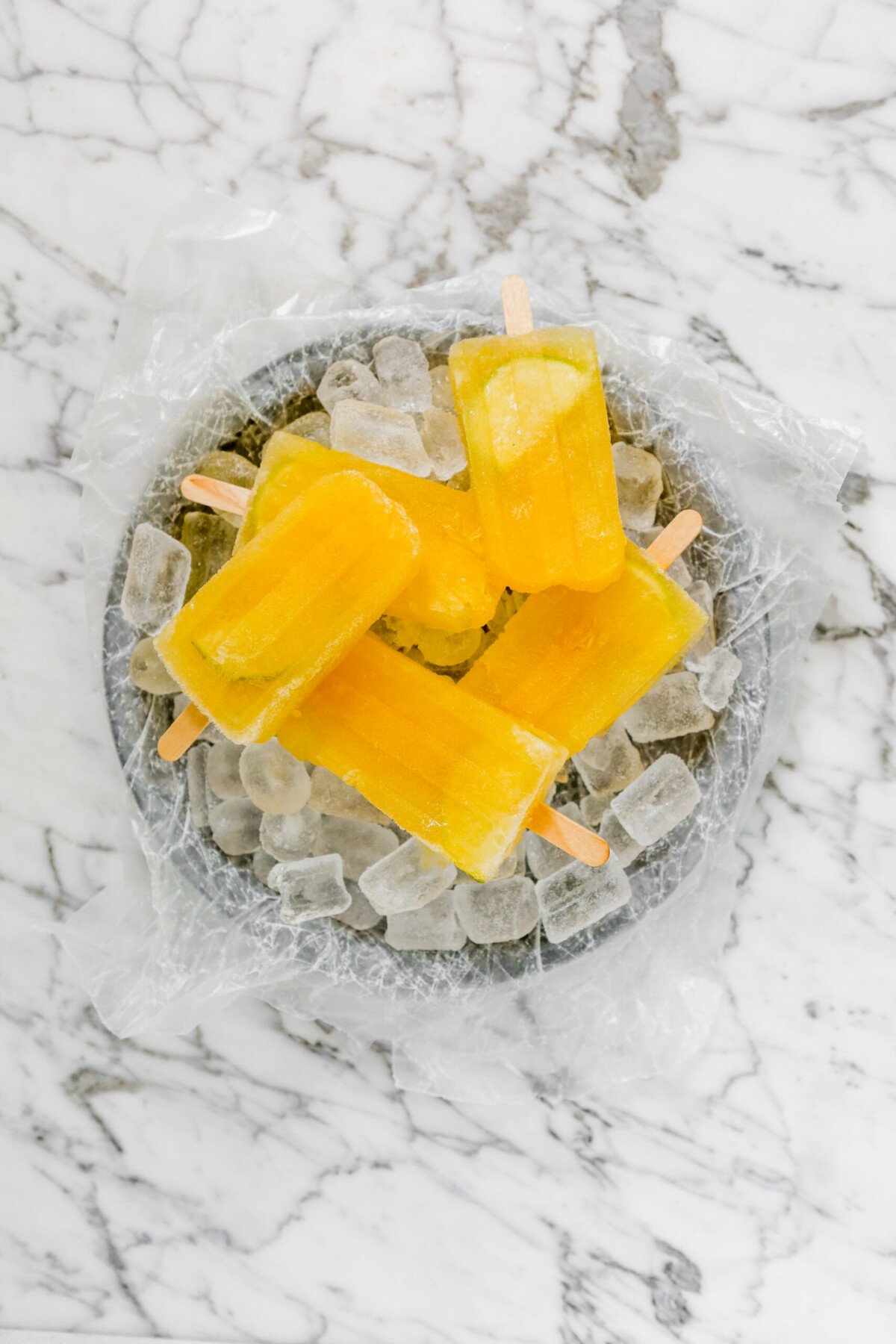 Bright yellow popsicles set on a gray plate with ice 