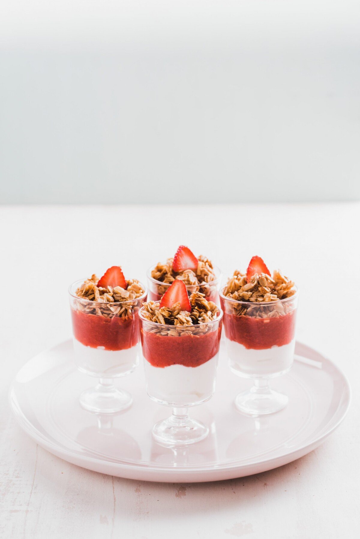 Yogurt and fruit parfaits with granola and strawberries set on a white plate