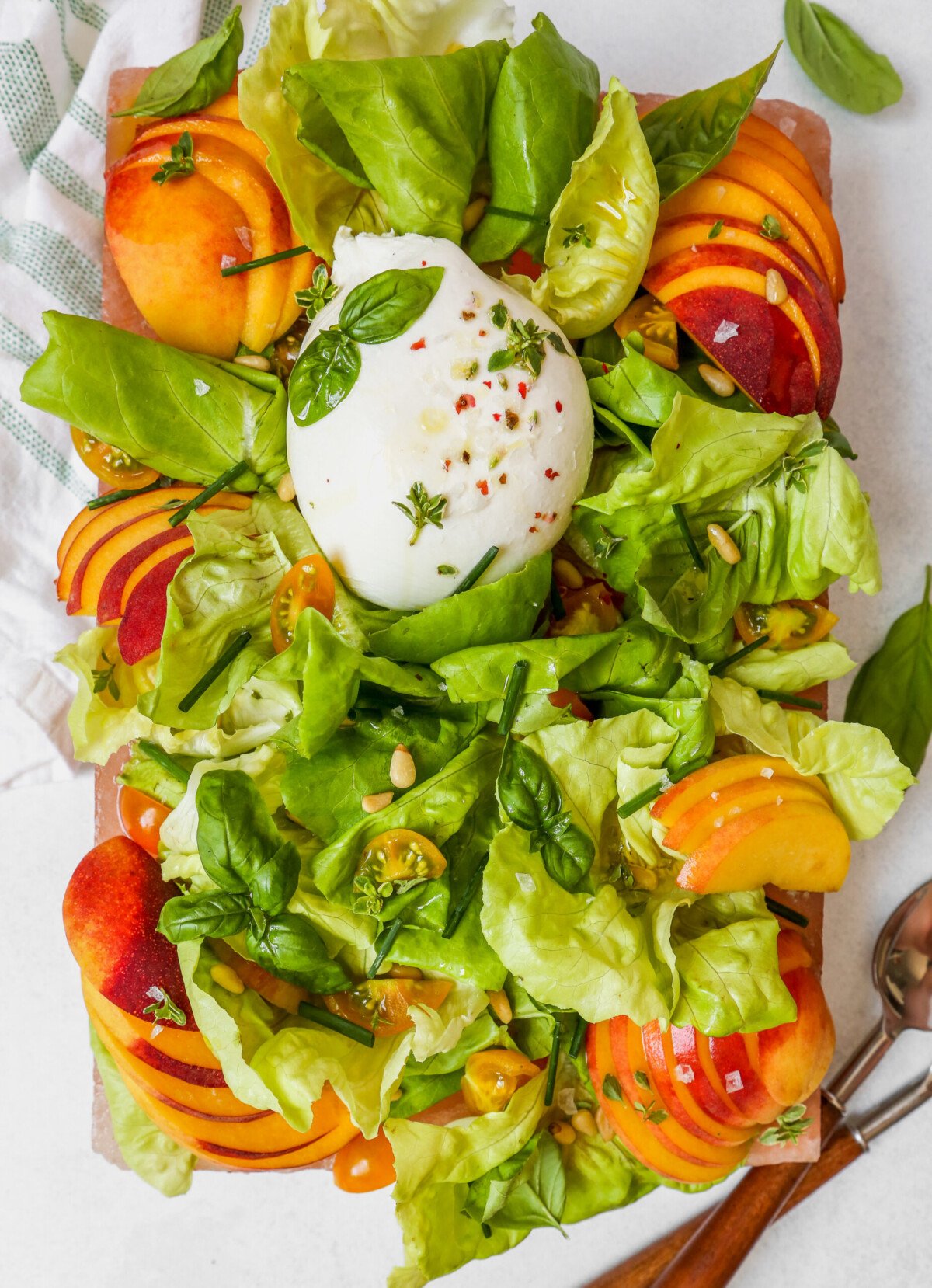 Simple summer salad with peaches, herbs, and burrata arranged on a pink platter, or salt block, set on a white surface.