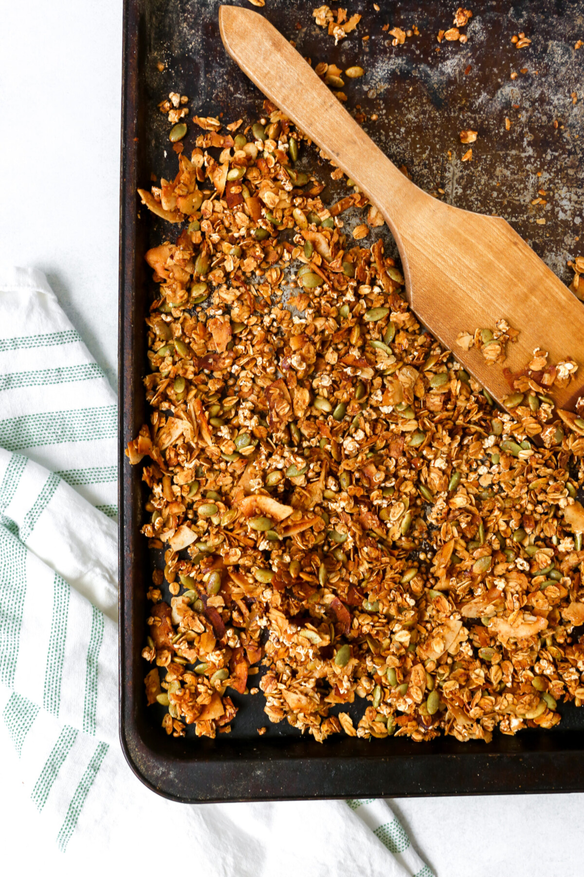 Homemade granola recipe on a black baking sheet with a white and green towel set to the side.
