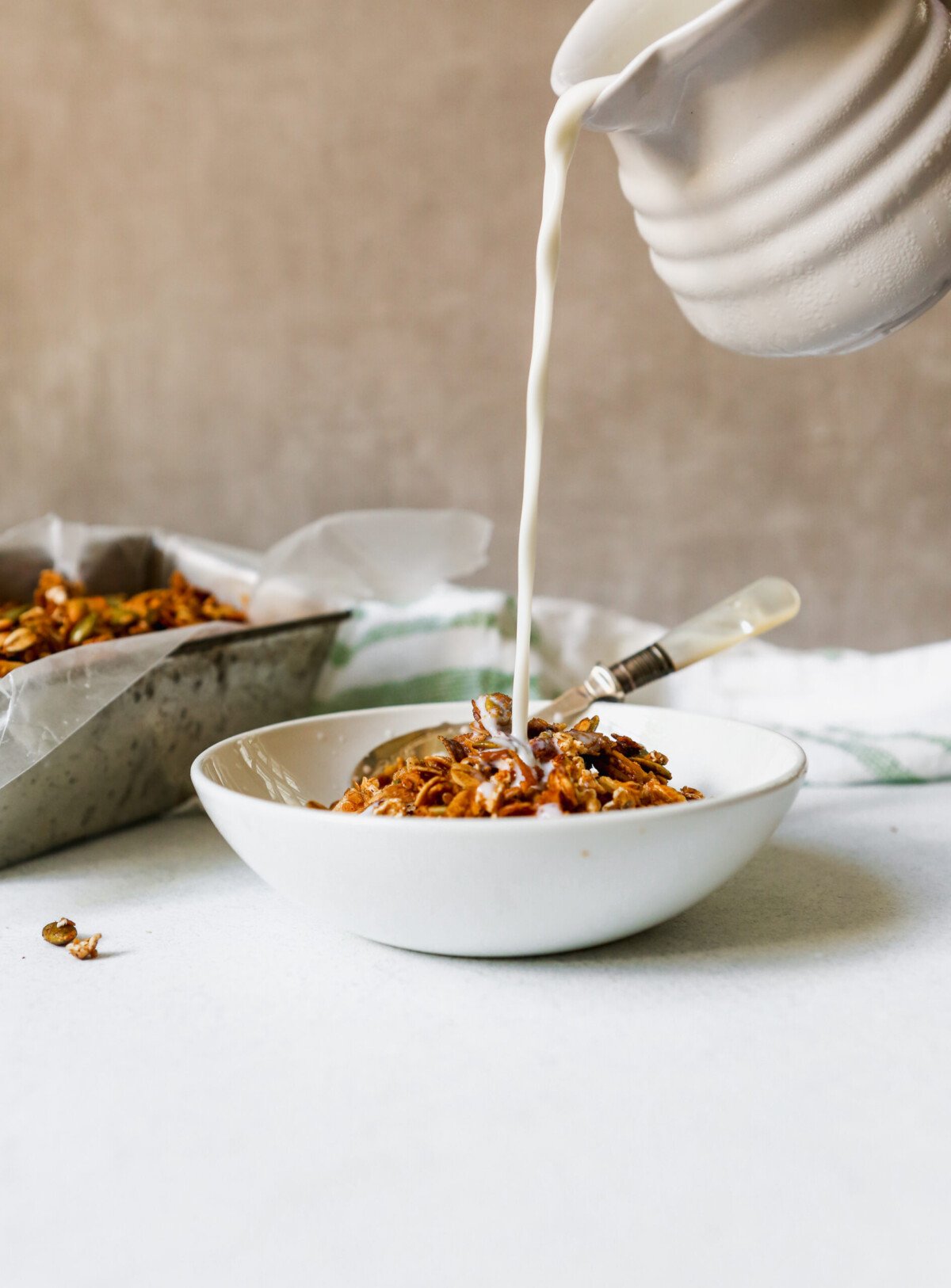 Homemade granola in a white bowl with milk pouring into bowl.