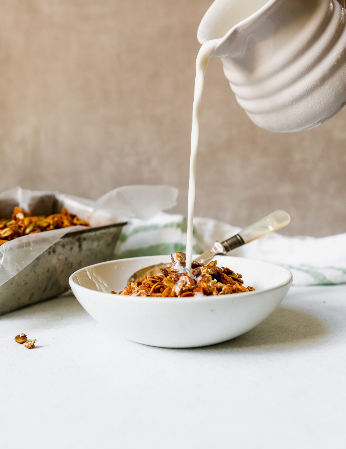Homemade healthy granola in a white bowl with milk pouring into it.
