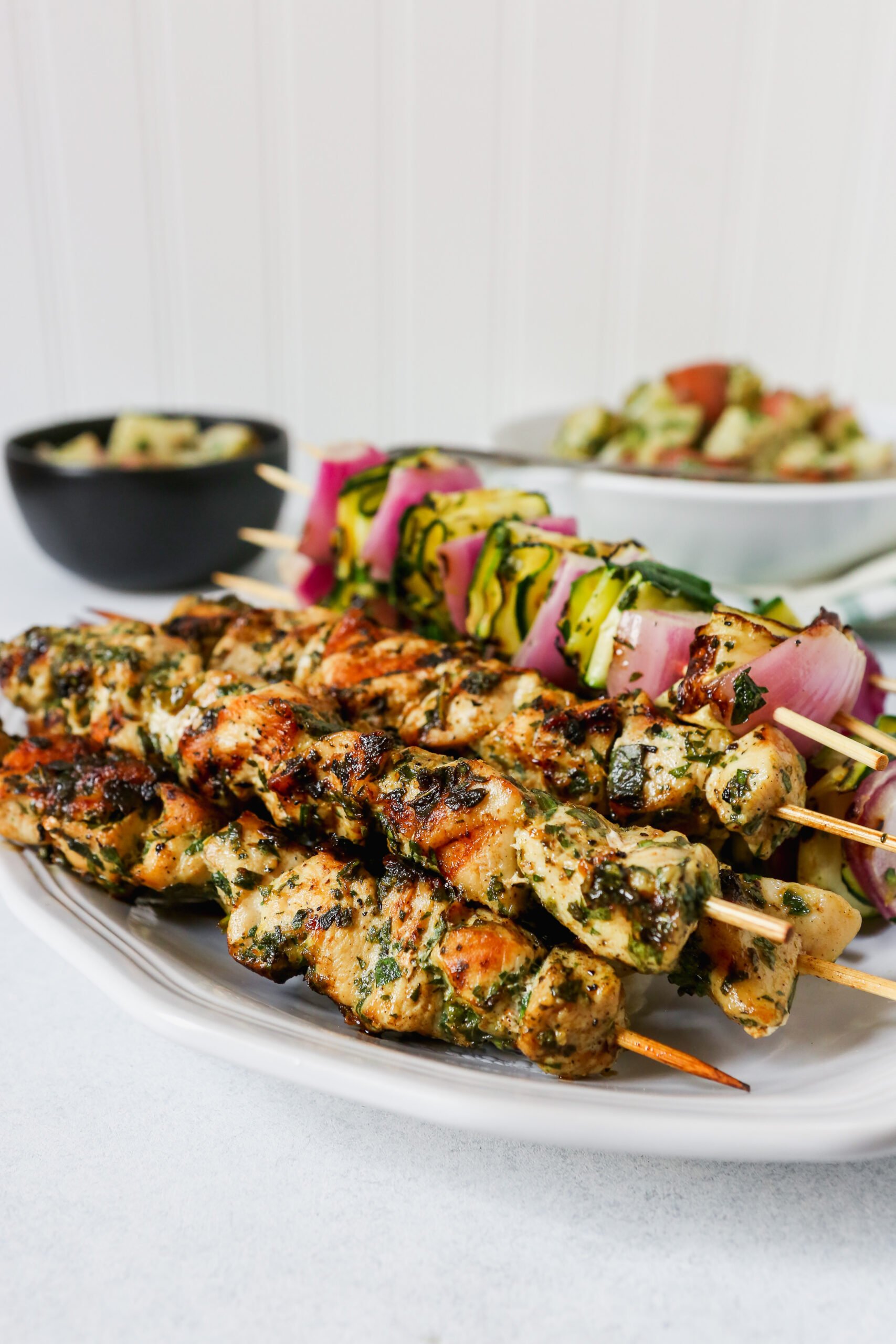 Chicken and vegetable skewers piled on a white platter with a green and white napkin.