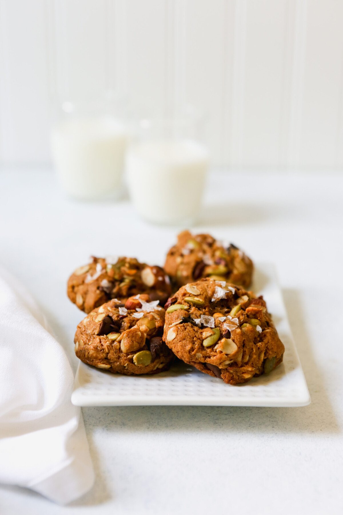Chunky trail mix cookies stacked on a white plate on a white surface.