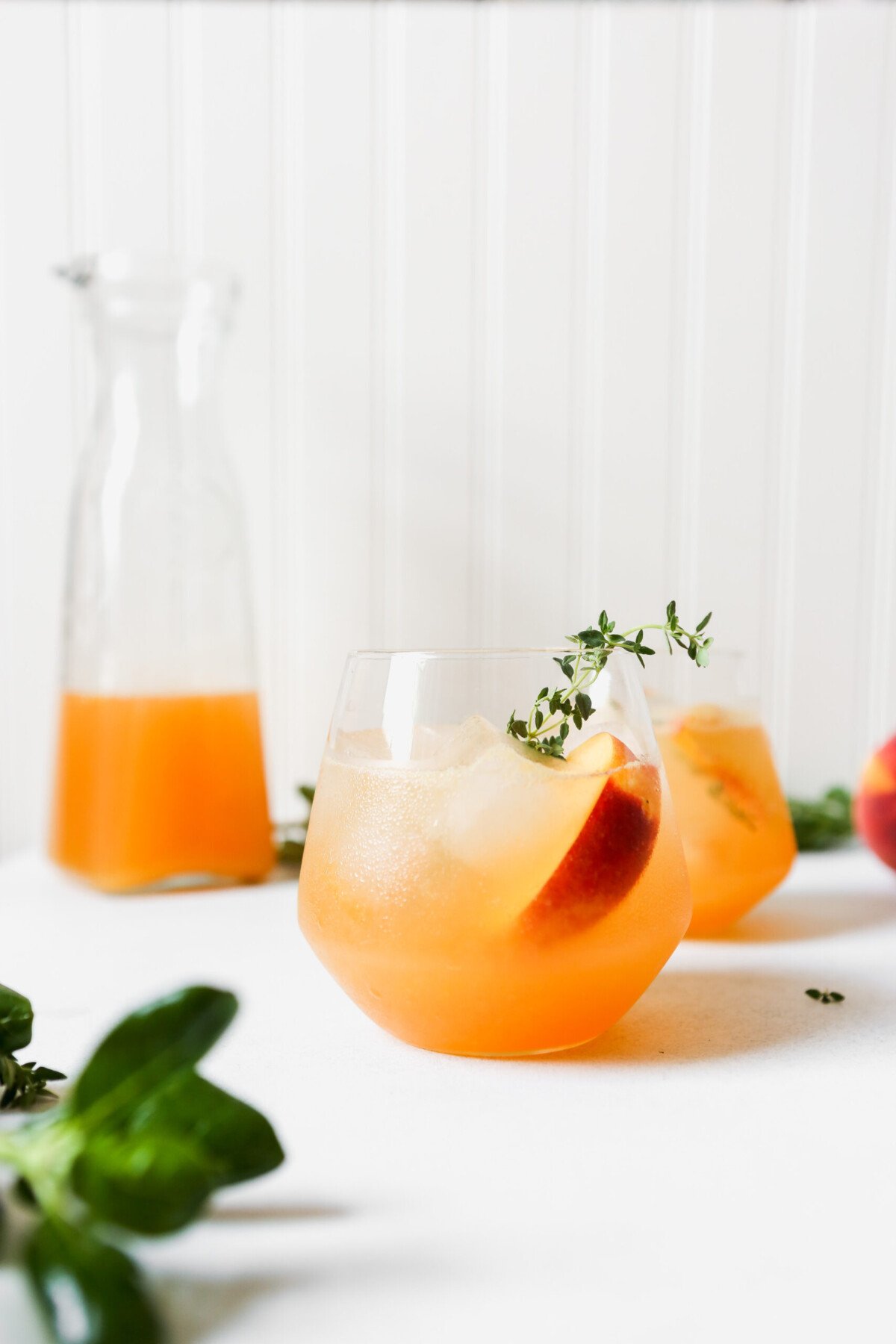 Peach and thyme cocktail photographed from overhead on a white surface. Fresh peach and thyme sprigs arranged around drink.