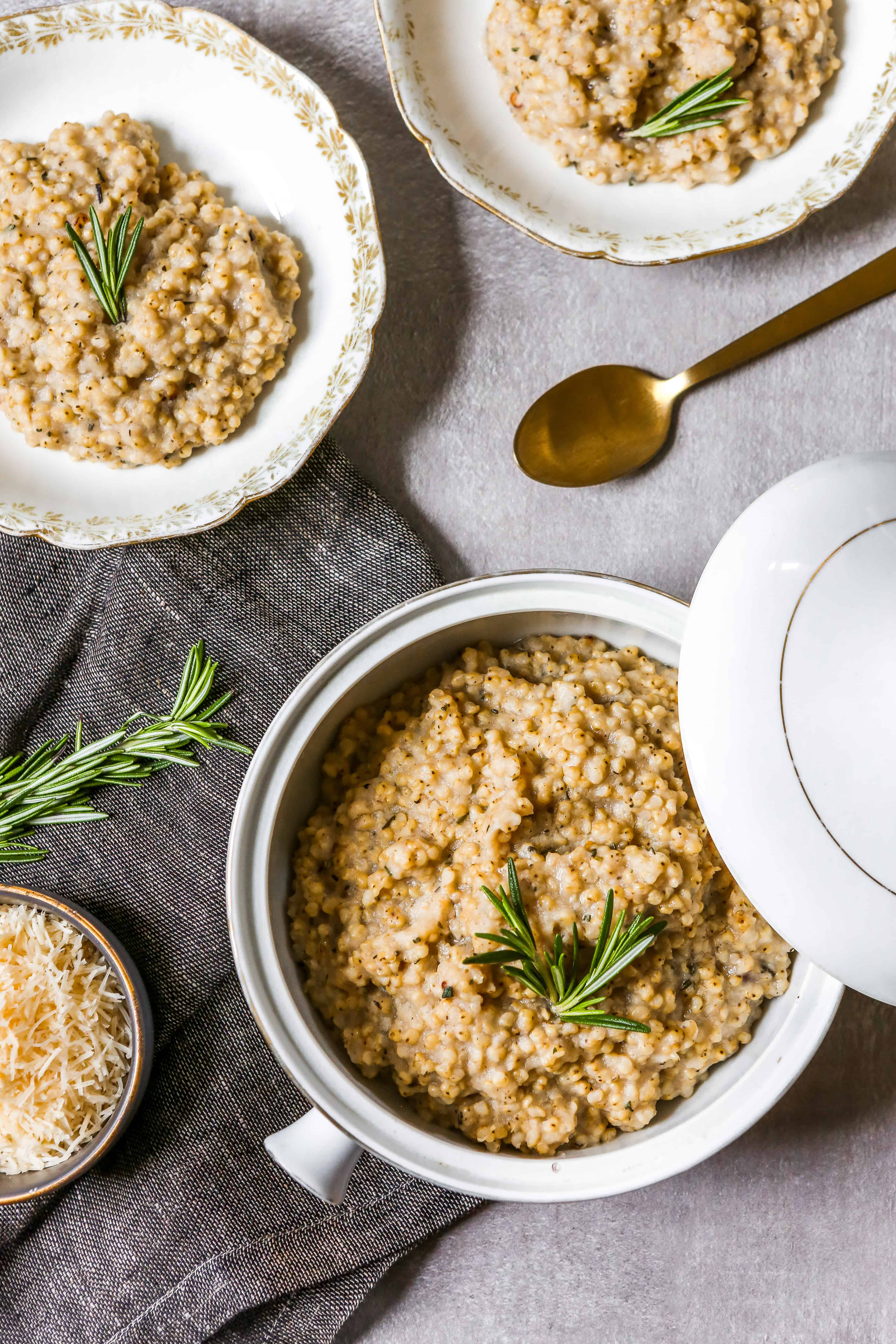 A white and gold bowl, filled with a serving or sorghum risotto and garnished with a sprig of rosemary
