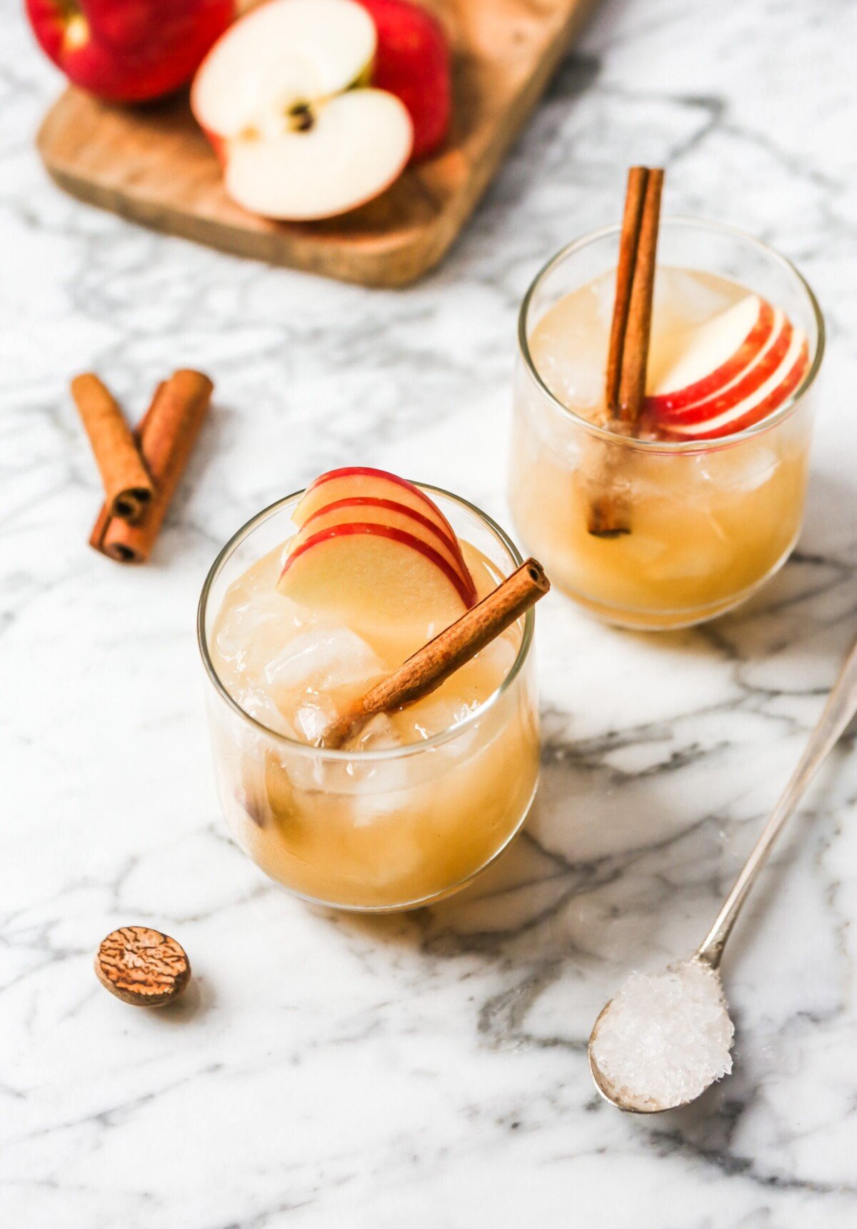 Apple bourbon cocktail on a white marble surface garnished with apple slices and cinnamon stick