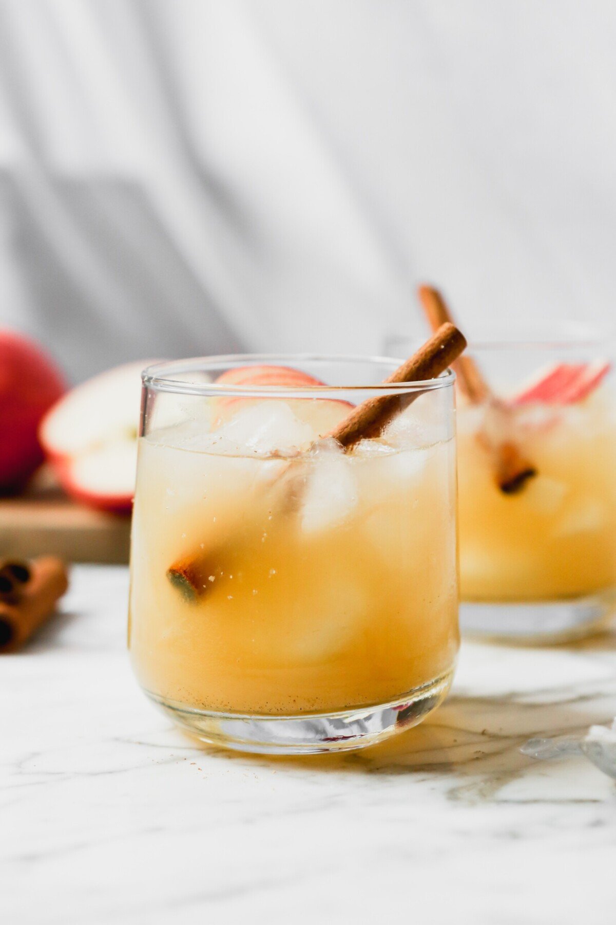 Apple bourbon cocktail on a white marble surface garnished with apple slices and cinnamon stick