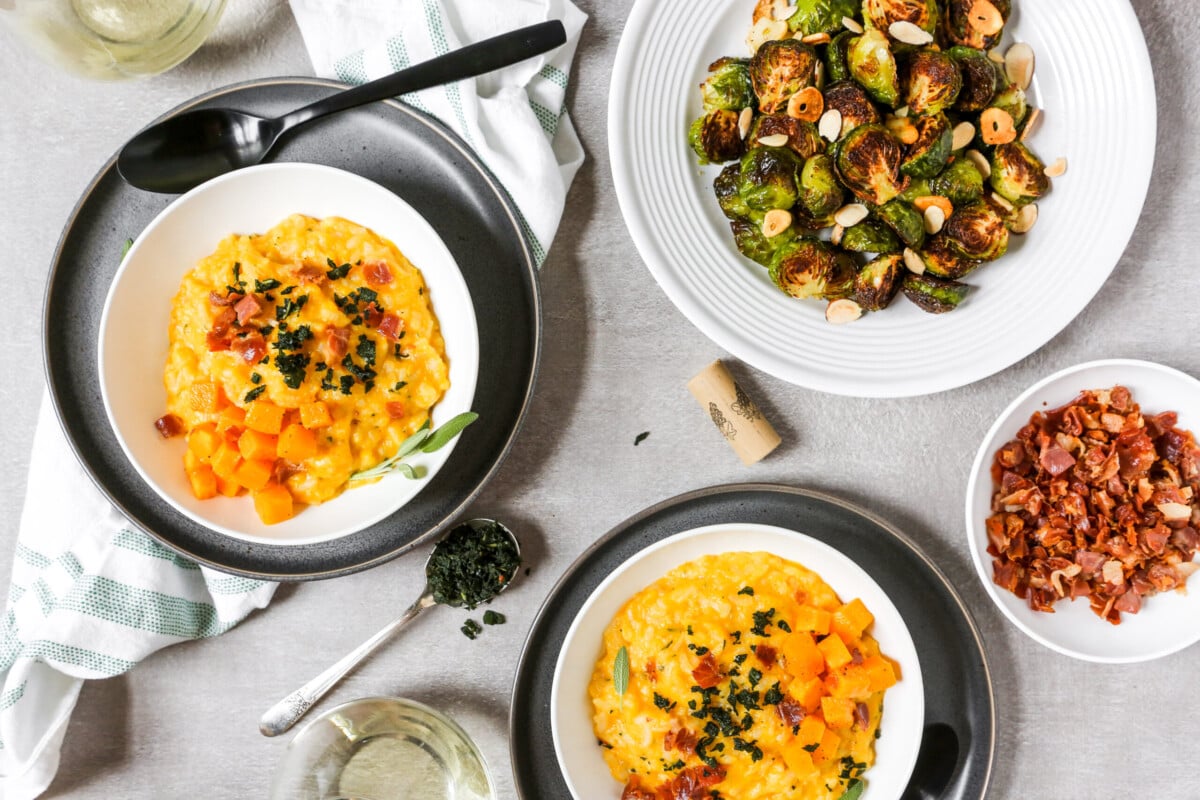 Dinner table with bowls of butternut squash risotto, roasted brussels sprouts, prosciutto, and wine.
