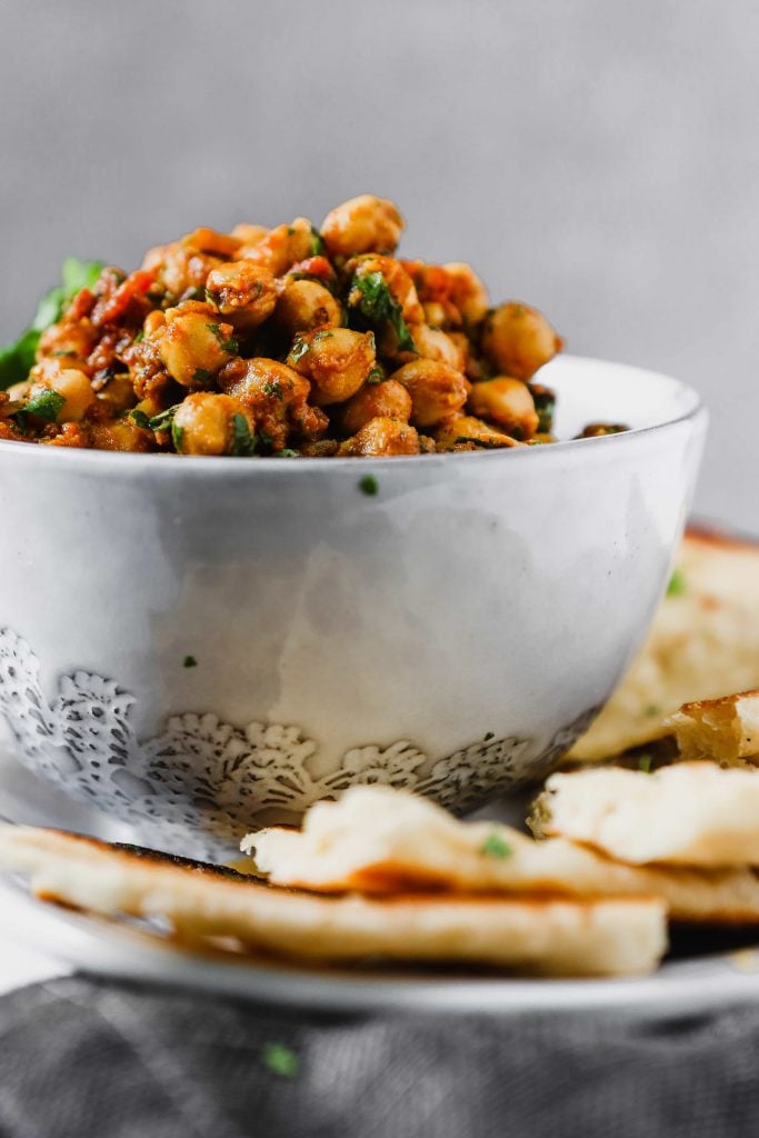 chickpeas and tomatoes in a white dish set on a white plate with homemade naan bread.