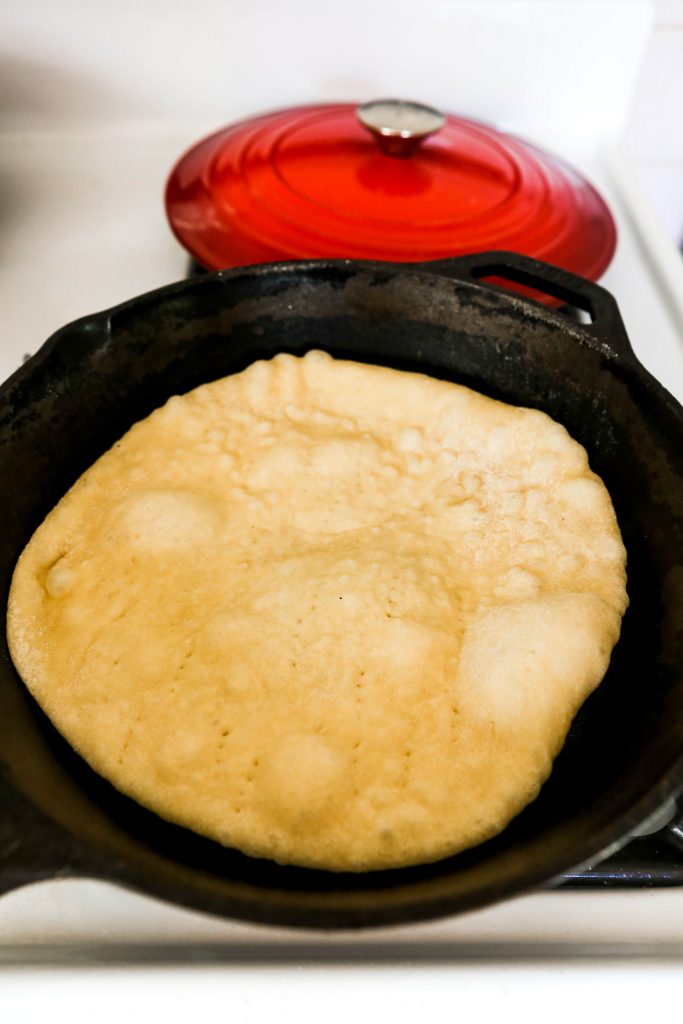Side angle of naan bread being cooked in a cast iron skillet 