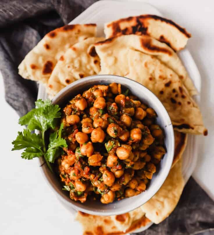 chickpeas and tomatoes in a white dish set on a white plate with homemade naan bread.