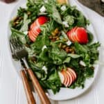 Photography of kale apple salad on a large white plate set on a white surface.