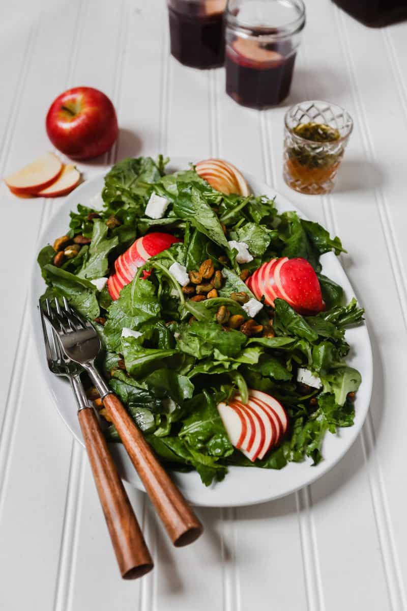 Photography of kale apple salad on a large white plate set on a white surface. 