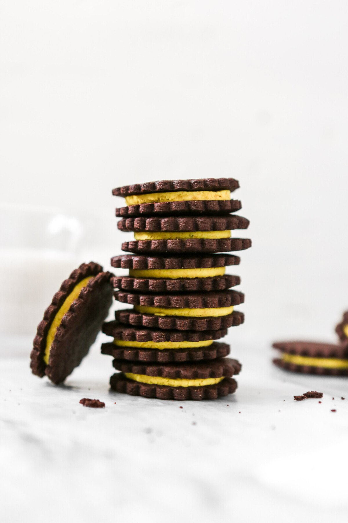 Photography of chocolate sandwich cookies with yellow frosting stacked on white marble. 