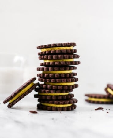 Photography of chocolate sandwich cookies with yellow frosting stacked on white marble.
