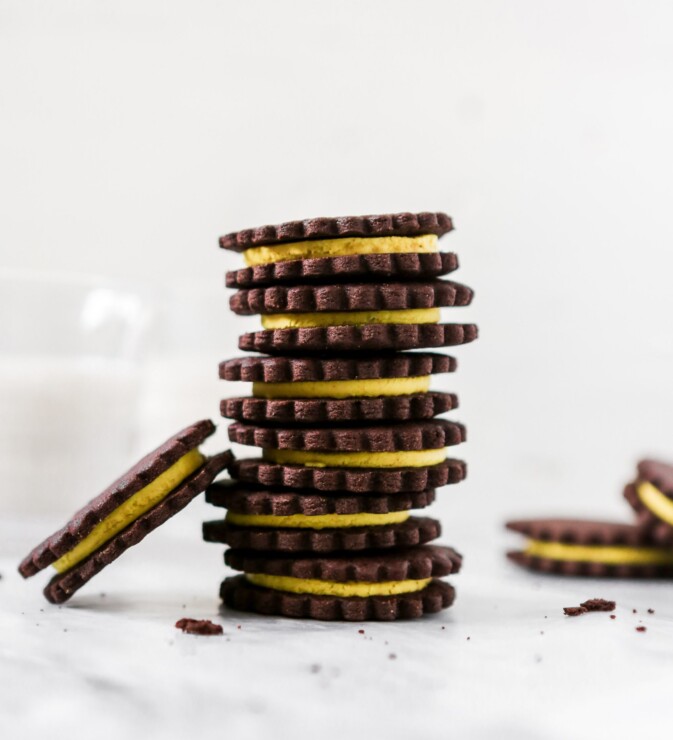 Photography of chocolate sandwich cookies with yellow frosting stacked on white marble.