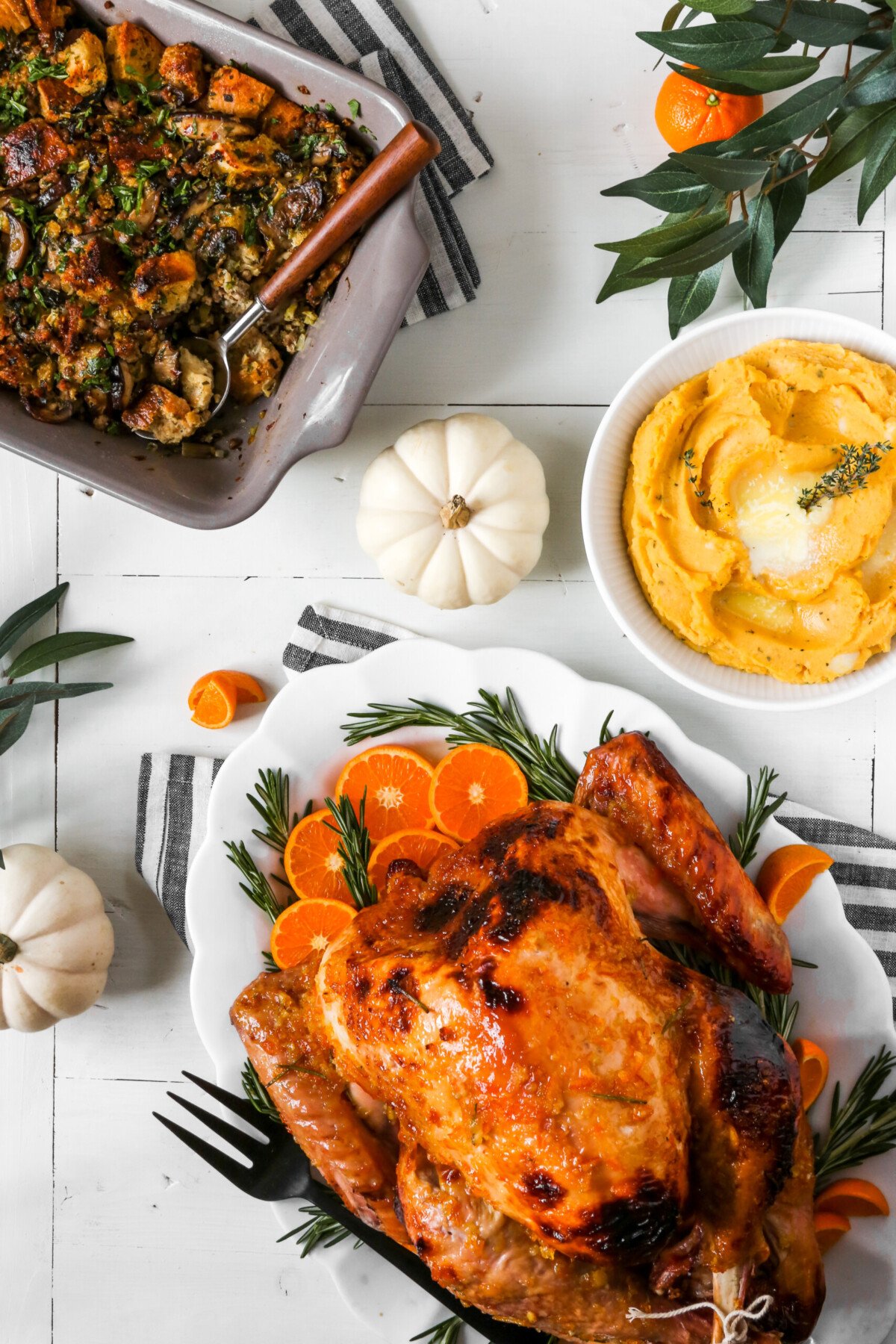 photograph of a Thanksgiving table scape and meal with a glazed roast turkey, stuffing, and mashed potatoes