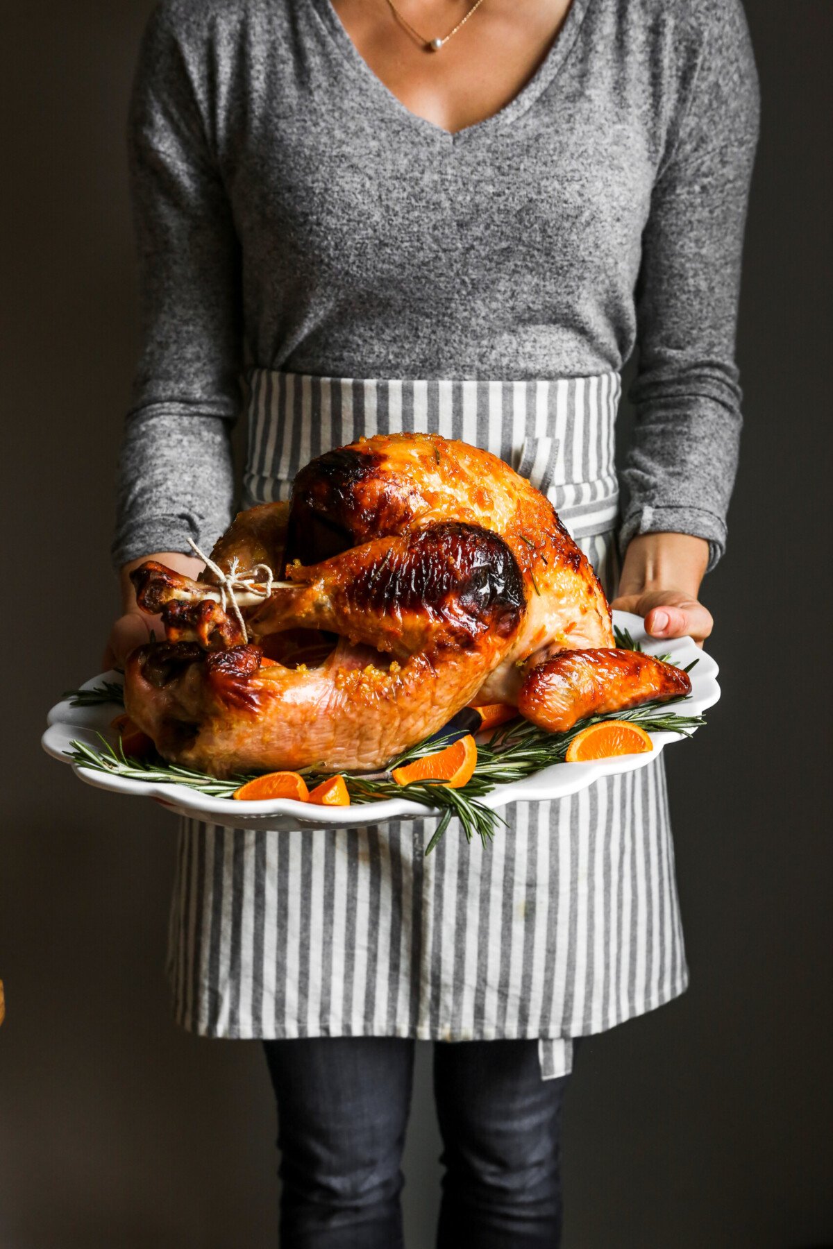 photograph of a whole glazed roast turkey on a large white platter held by someone in an apron