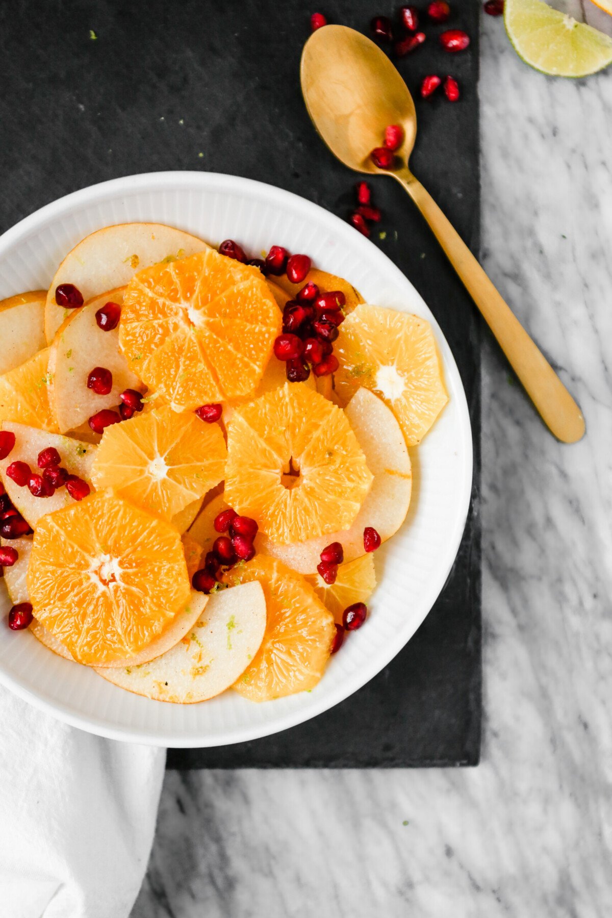 Photograph of winter citrus fruit salad with pomegranate seeds set in a white bowl on a marble table.