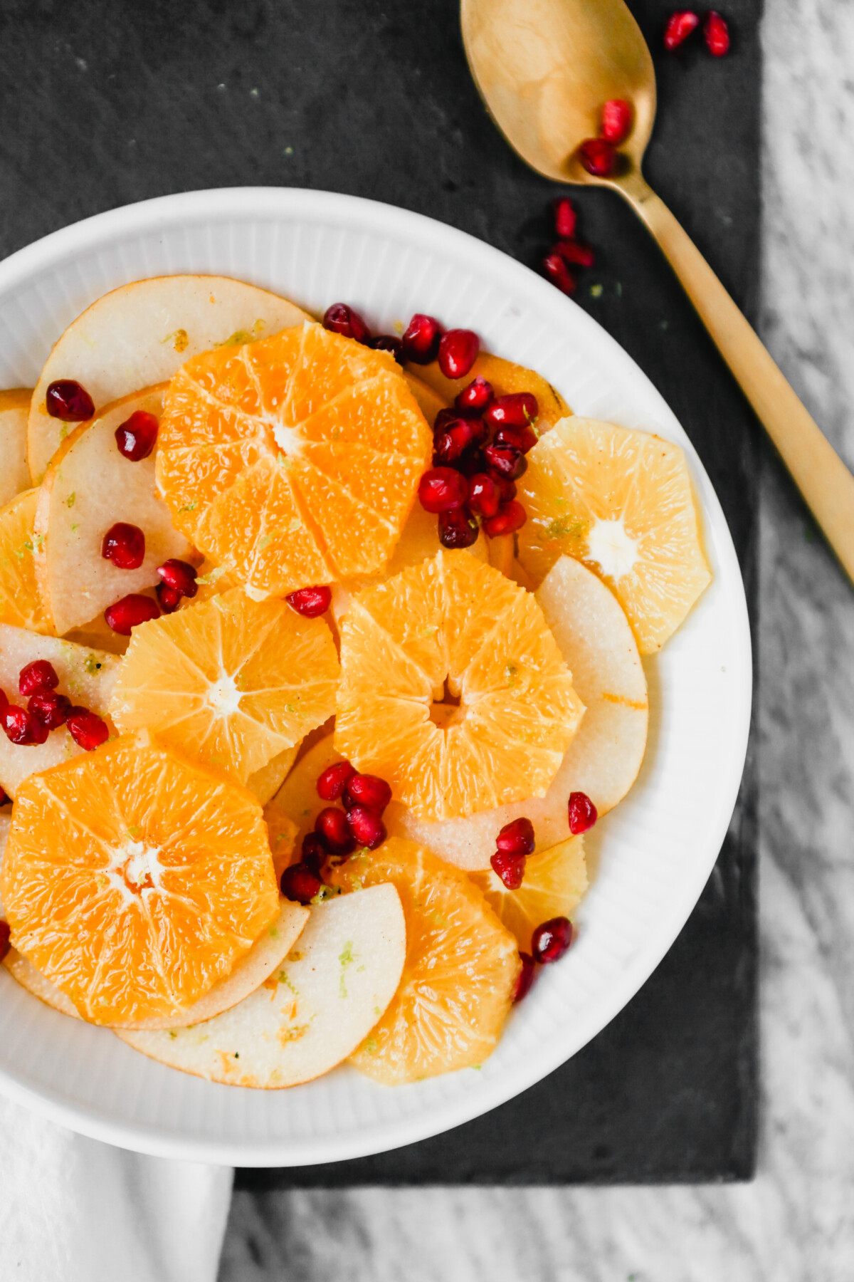 Photograph of winter citrus fruit salad with pomegranate seeds set in a white bowl on a marble table.
