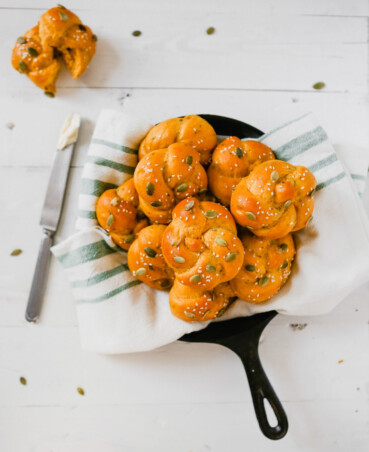 photograph of pumpkin sage challah rolls in a kitchen towel set in a cast-iron skillet