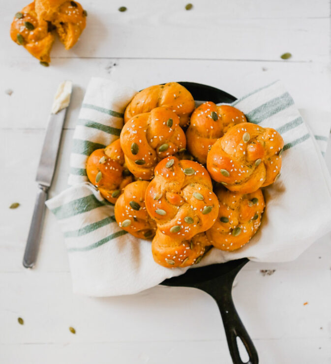 photograph of pumpkin sage challah rolls in a kitchen towel set in a cast-iron skillet