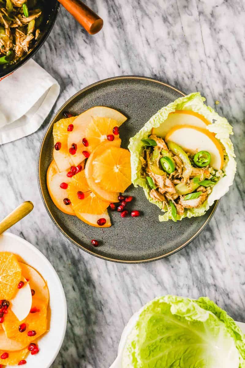Photograph of table with Chinese turkey lettuce wraps on a gray plate with fruit salad.