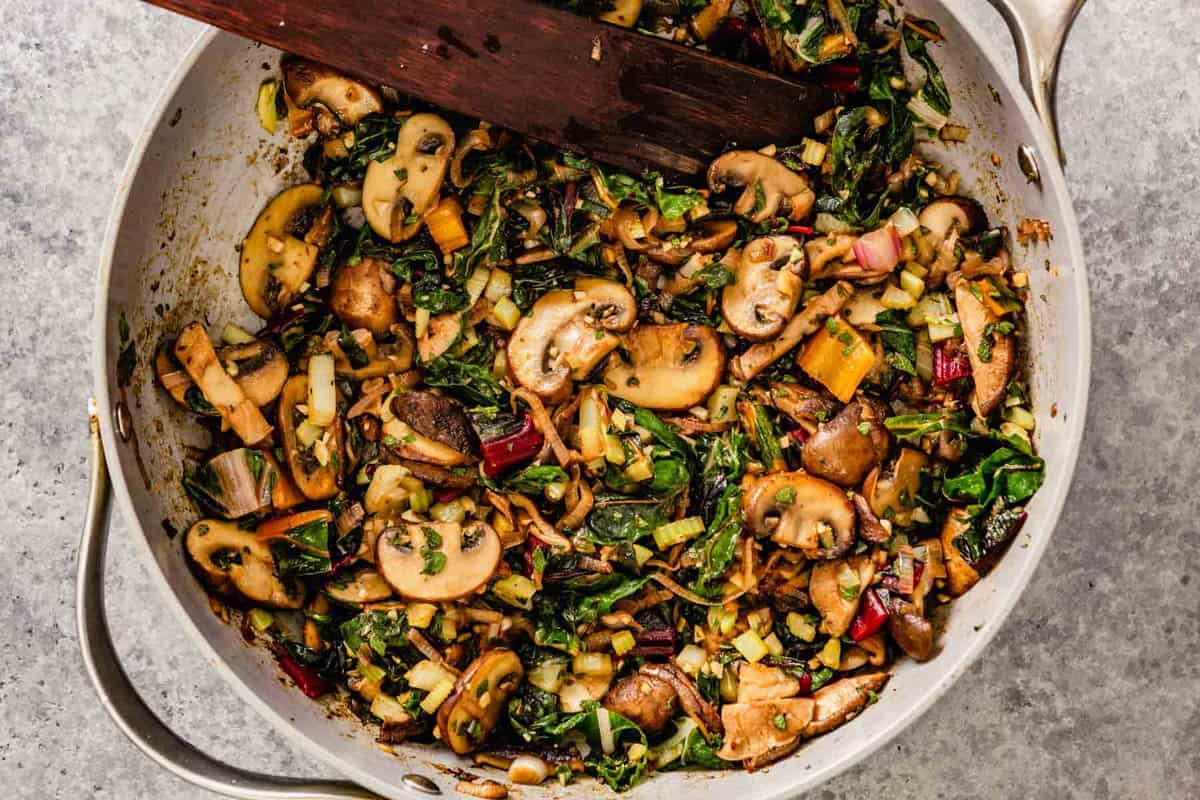 mushrooms, chard, and celery cook and in a gray skillet