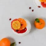 Photography of mini pavlova topped with pink cranberry curd, citrus fruit and spices.