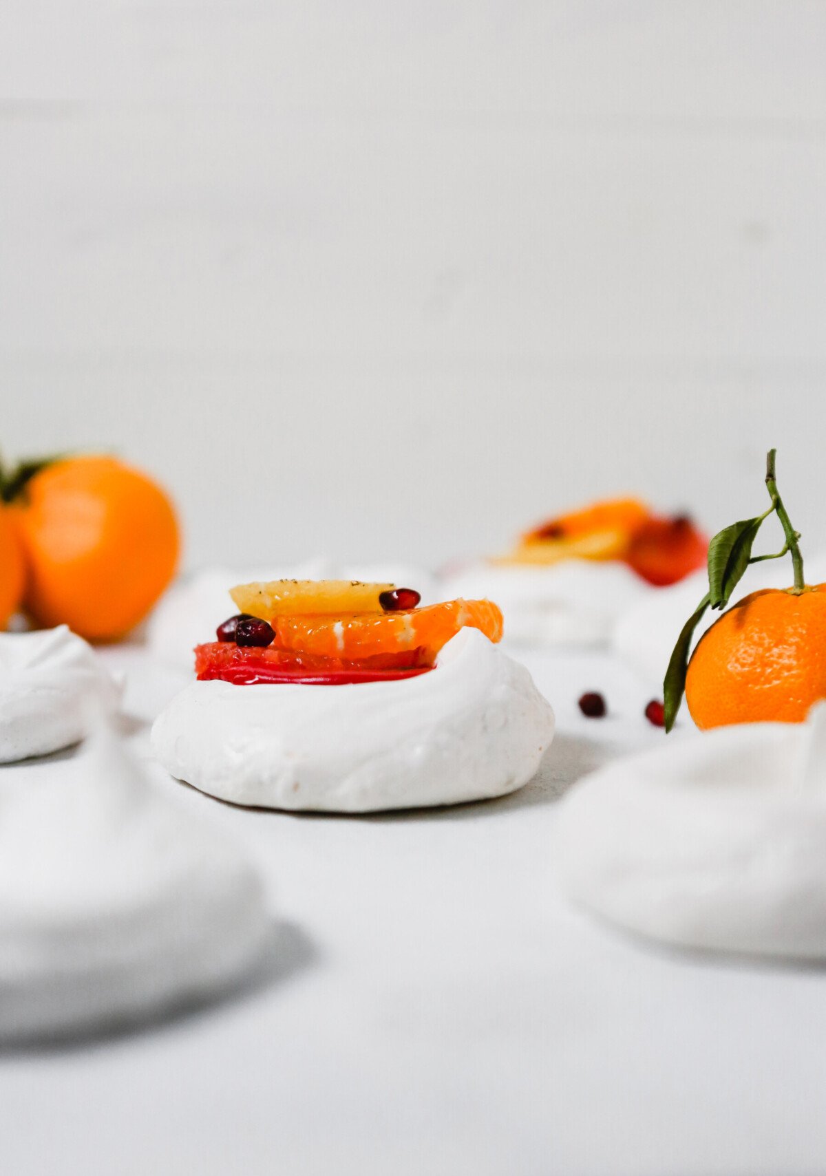 Photography of mini pavlova topped with pink cranberry curd, citrus fruit and spices.