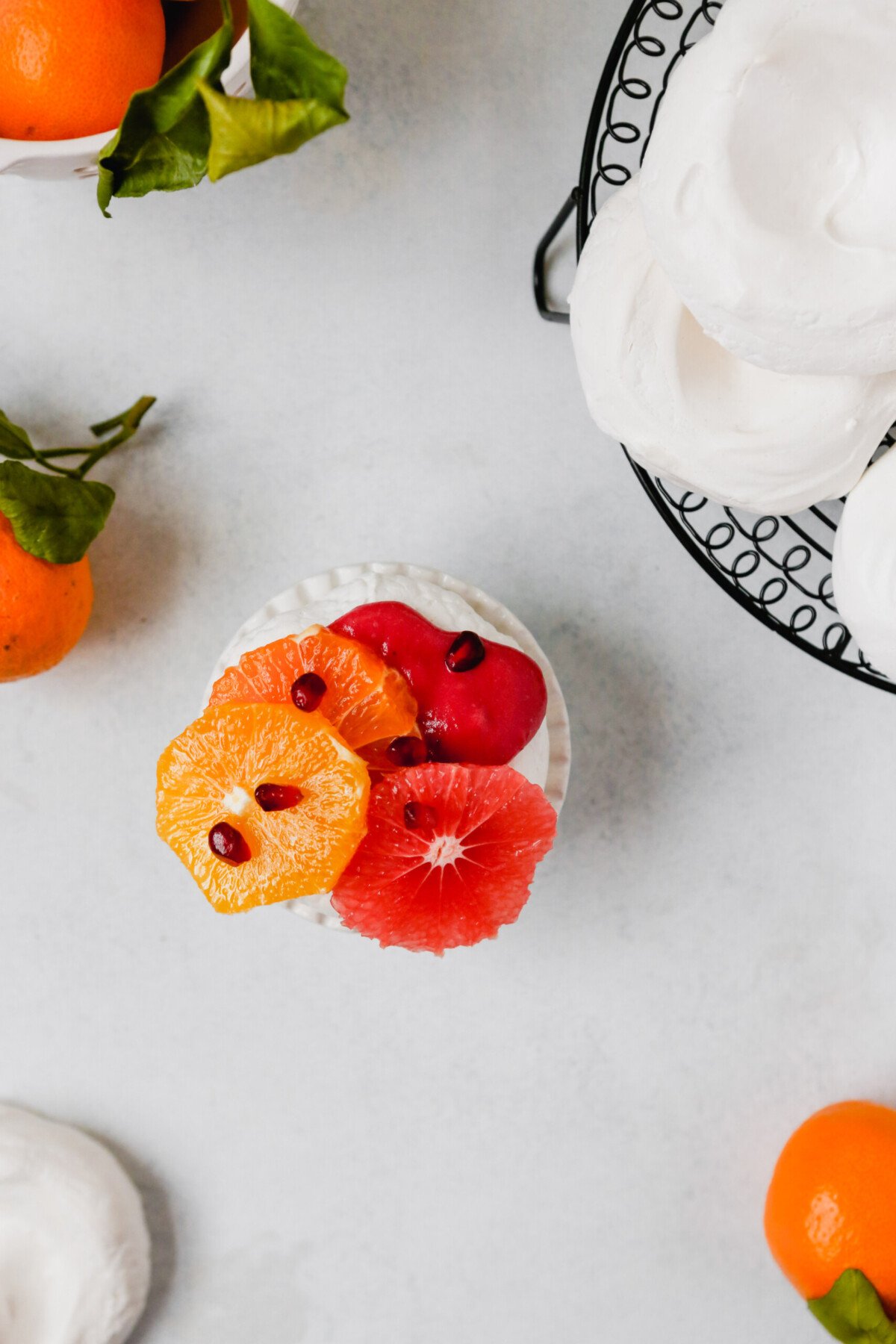 Photography of mini pavlova topped with pink cranberry curd, citrus fruit, pomegranate seeds and spices.