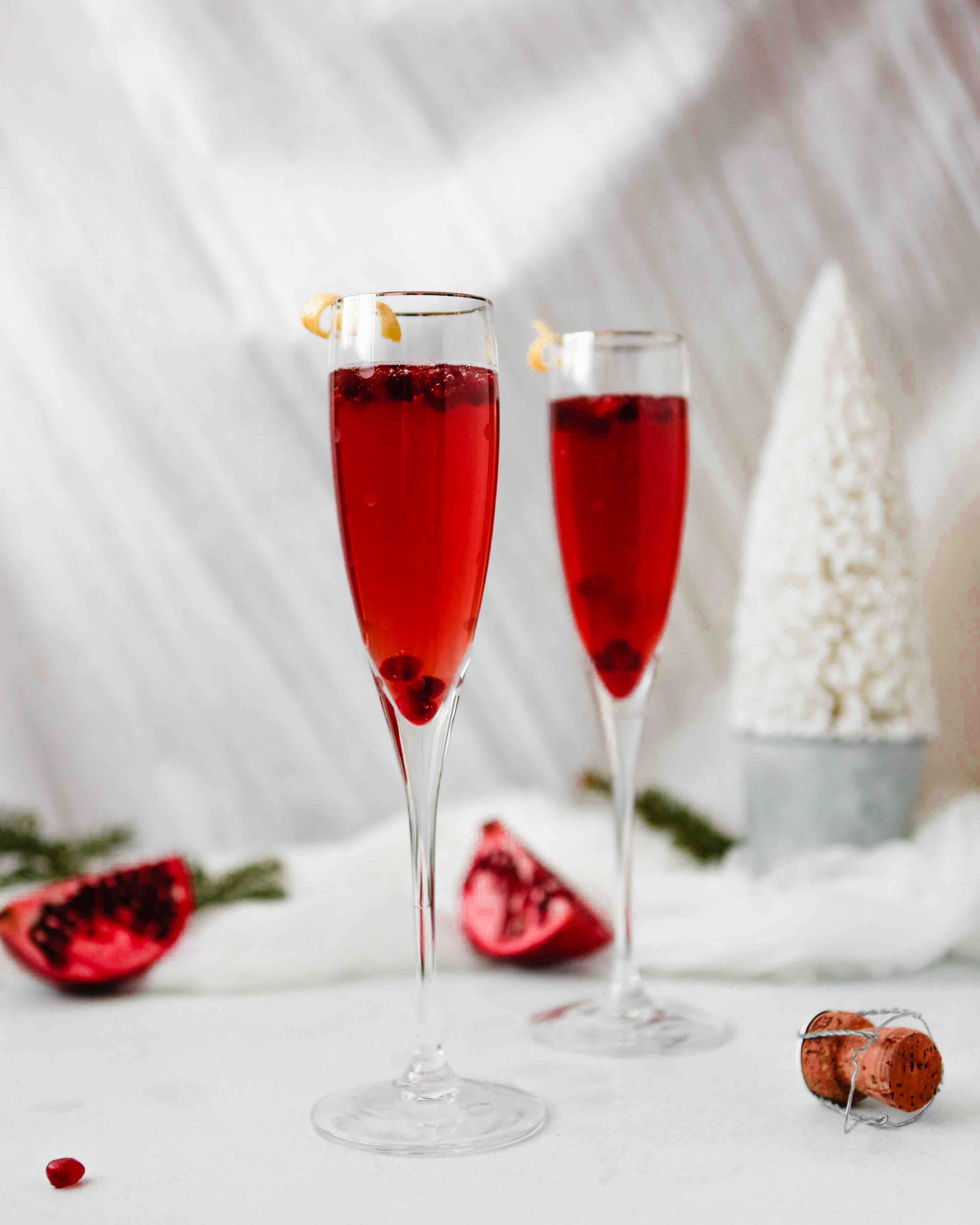 Photograph of pomegranate kir royale cocktail in two flutes, cheersing