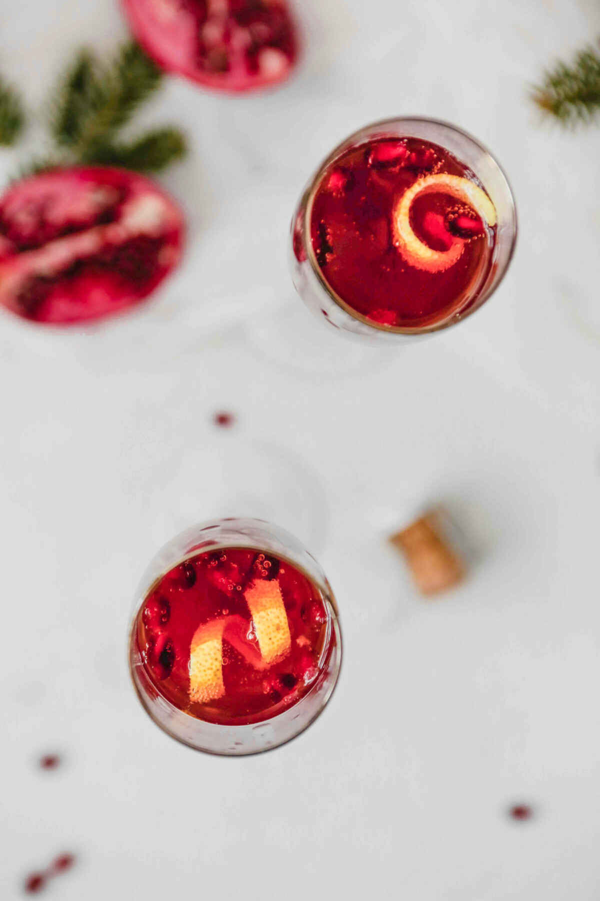 Photograph of pomegranate kir royale cocktail on a white table with holiday decorations in background