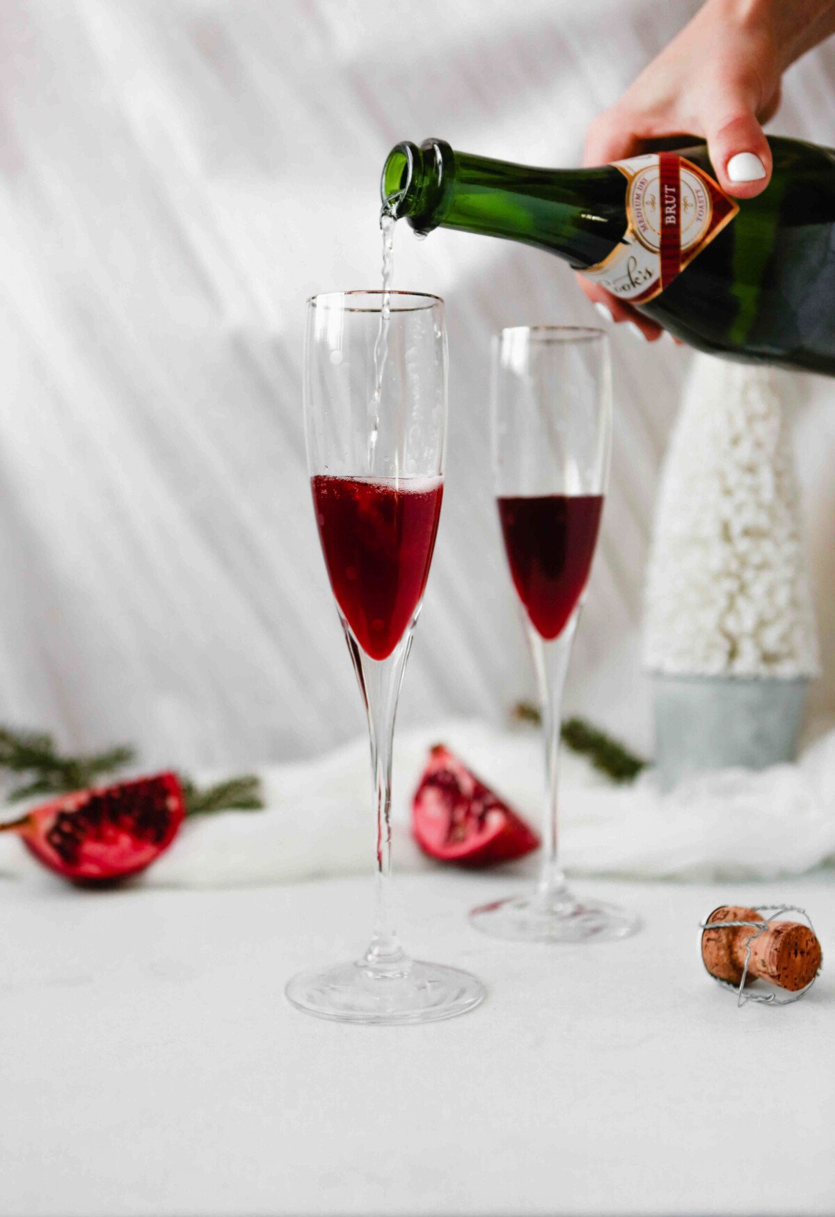Photograph of sparkling wine being poured into champagne flutes with pomegranate liqueur