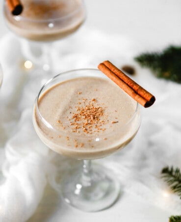 Photograph of homemade eggnog in a coupr glass set on a white wooden table.