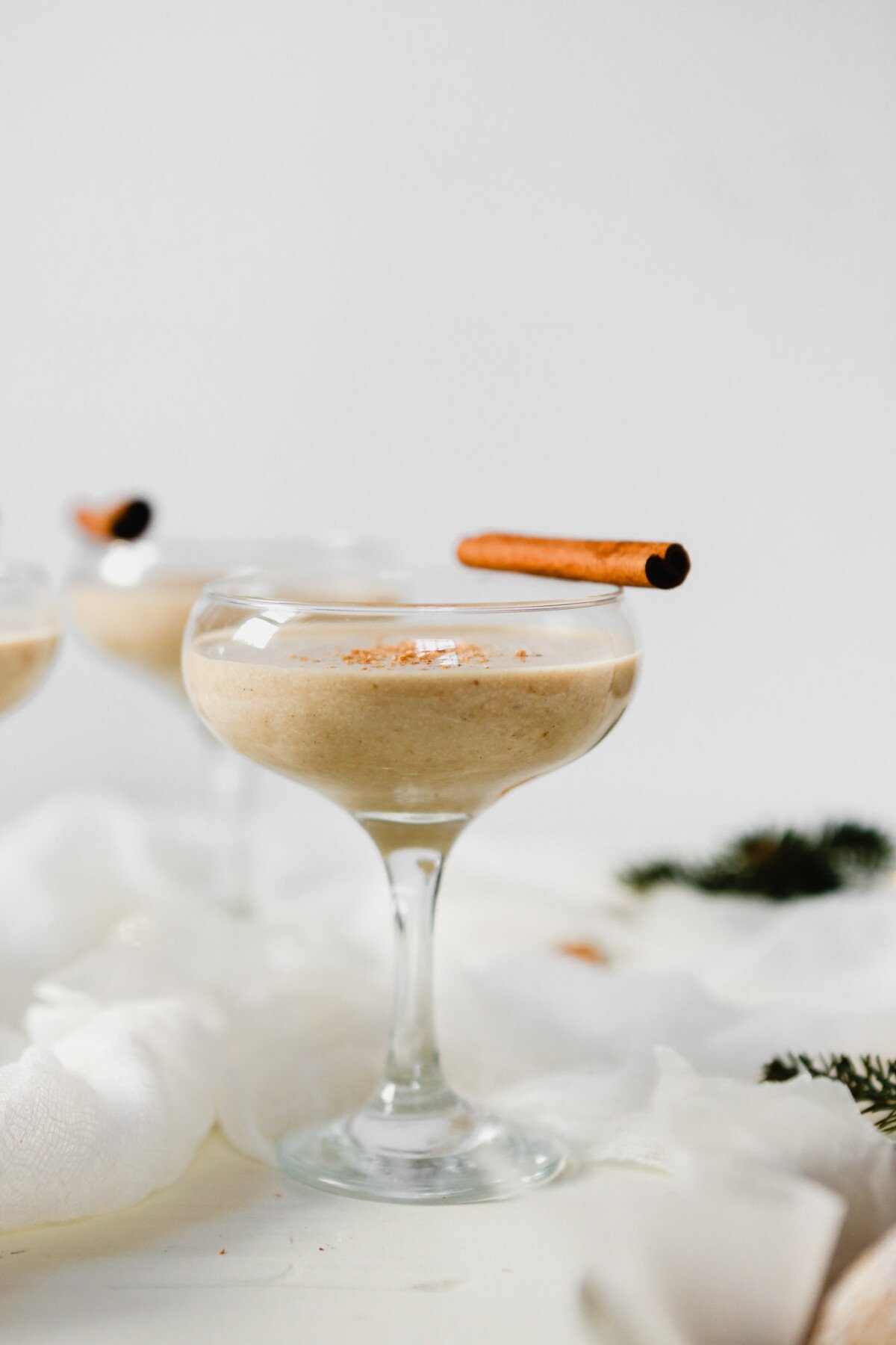 Photograph of homemade eggnog in a coupr glass set on a white wooden table.