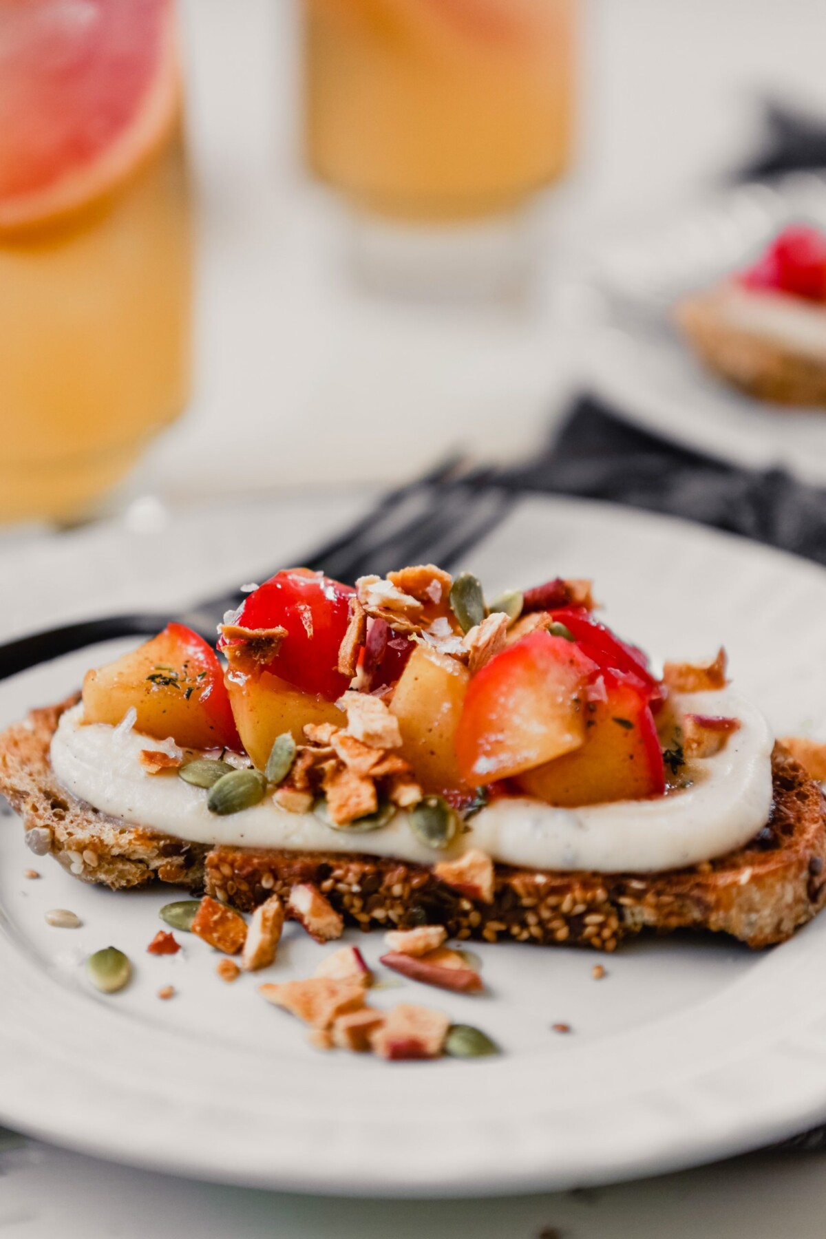 Photograph of wholegrain bread topped with ricotta, sauteed apples, and honey on a white plate