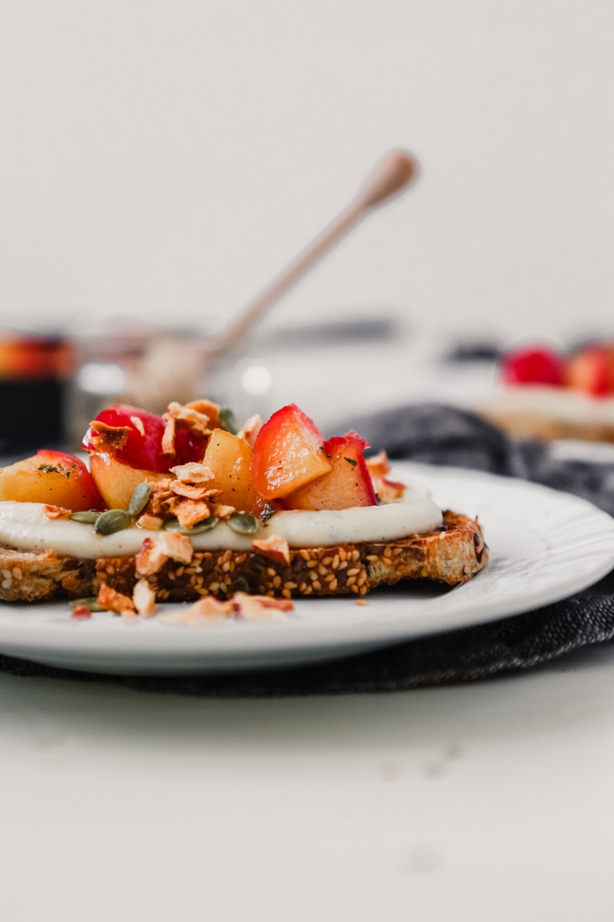 Photograph of wholegrain bread topped with ricotta, sauteed apples, and honey on a white plate