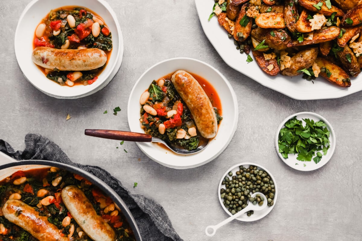Overhead photograph of bowls filled with kale, tomatoes, beans and chicken sausage