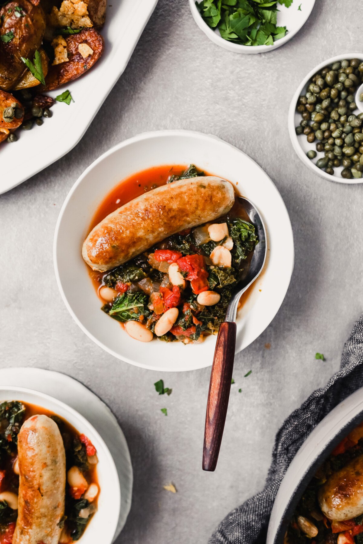 Overhead photograph of bowls filled with kale, tomatoes, beans and chicken sausage