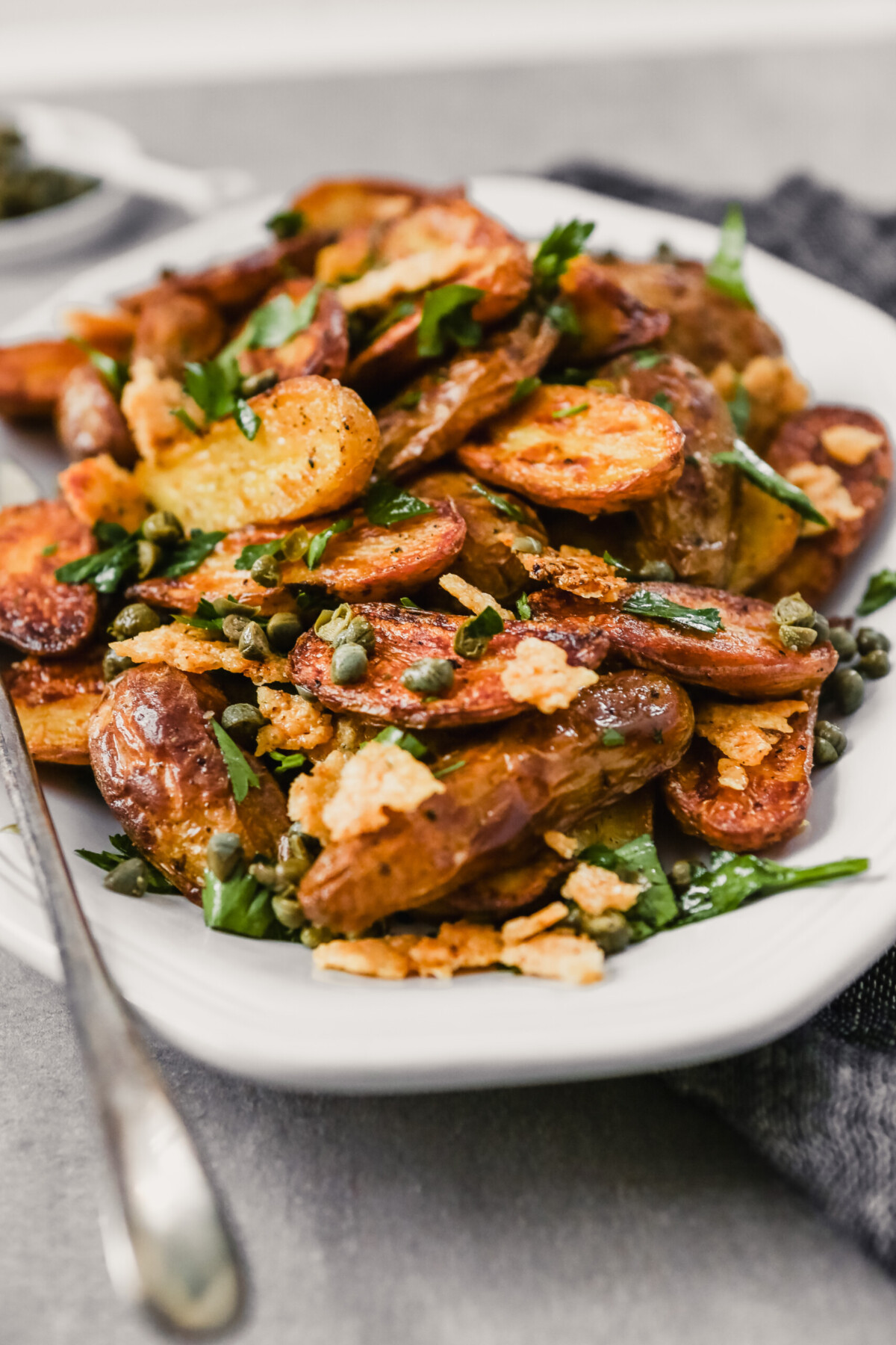 Photograph of crispy fingerling potatoes on a white oval plate set on a gray table. 