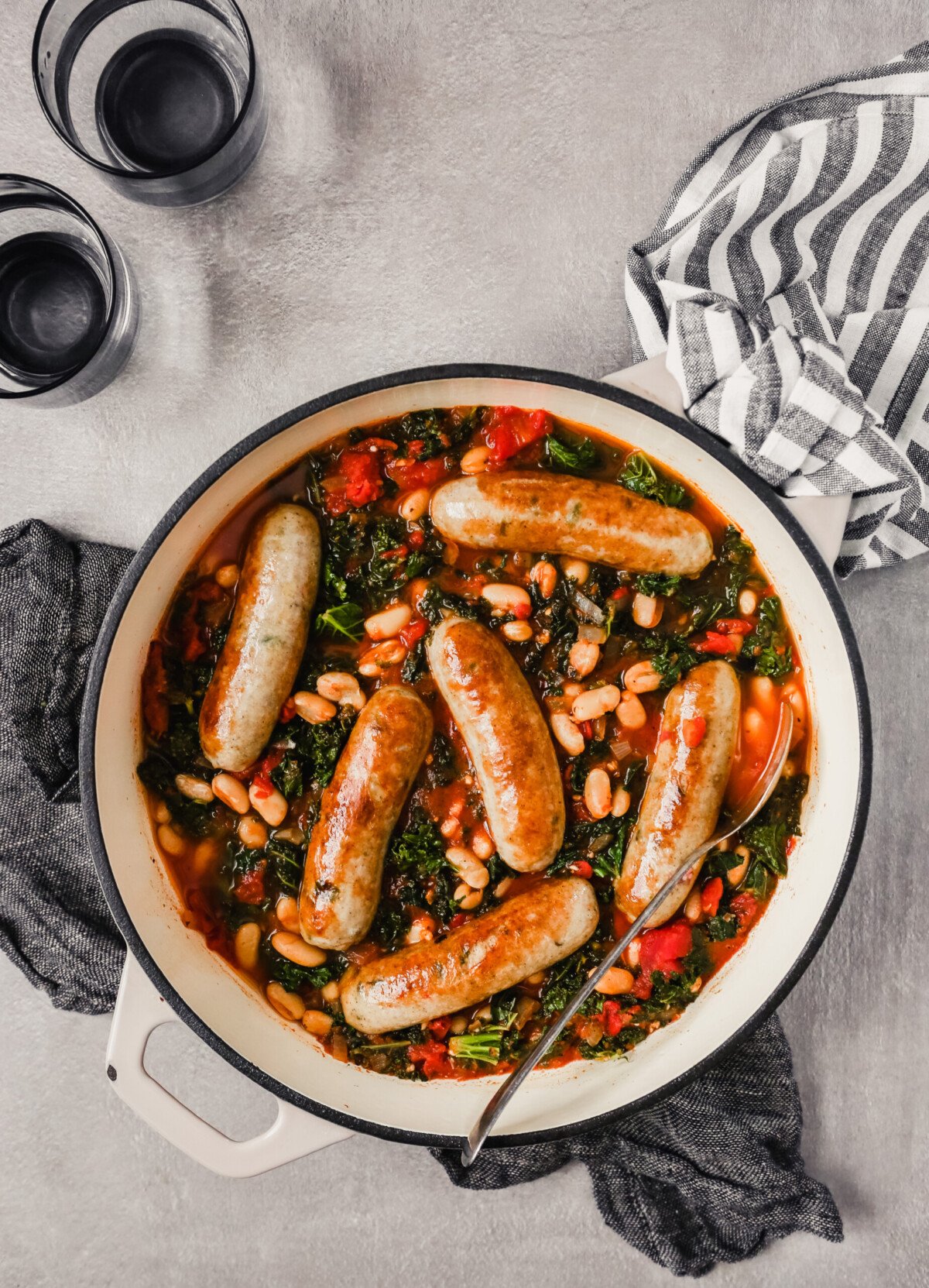 Overhead photograph of a Dutch oven filled with Italian chicken sausages stewed in tomatoes, kale and white beans
