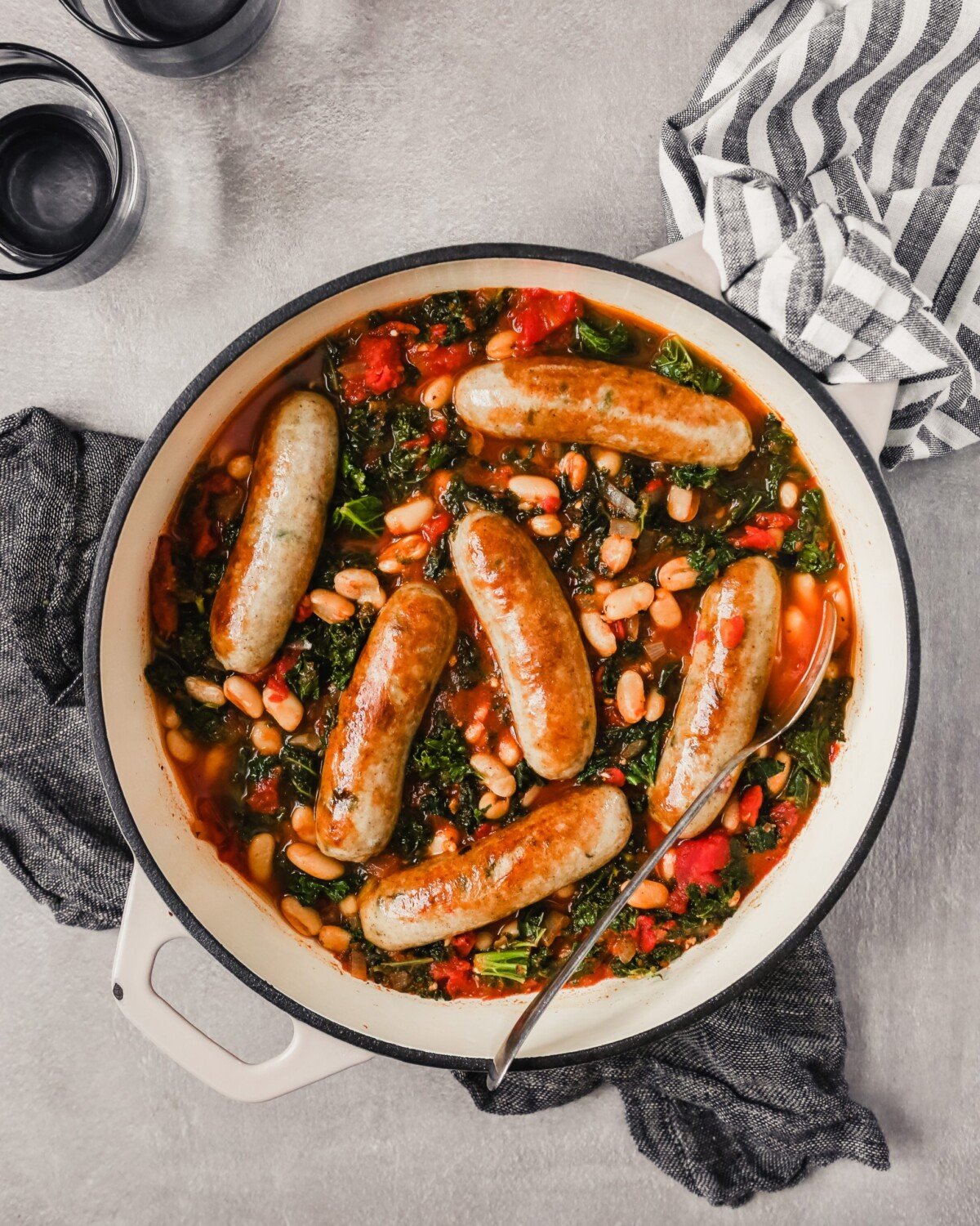 Overhead photograph of a Dutch oven filled with Italian chicken sausages stewed in tomatoes, kale and white beans